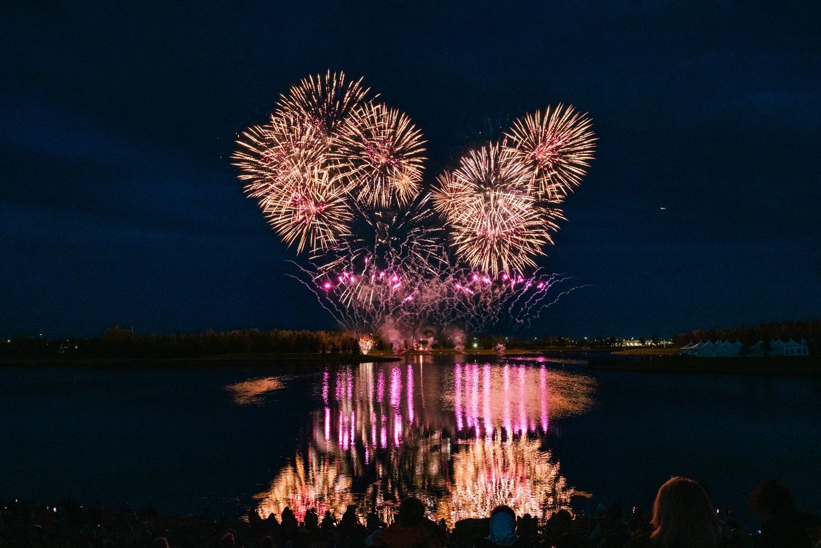 Fireworks bursting in pink and gold over a lake at night, reflected in the water, a fitting picture of the holiday events in Westlake FL and the villages nearby