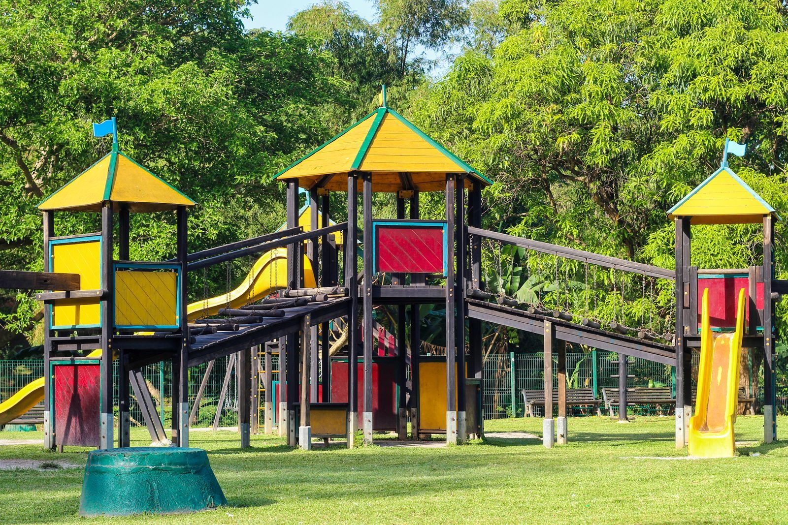 A large wooden playground with slides and yellow roofs on a green lawn ringed by trees; neighborhood parks are among the simple things to do in Westlake, Florida with children